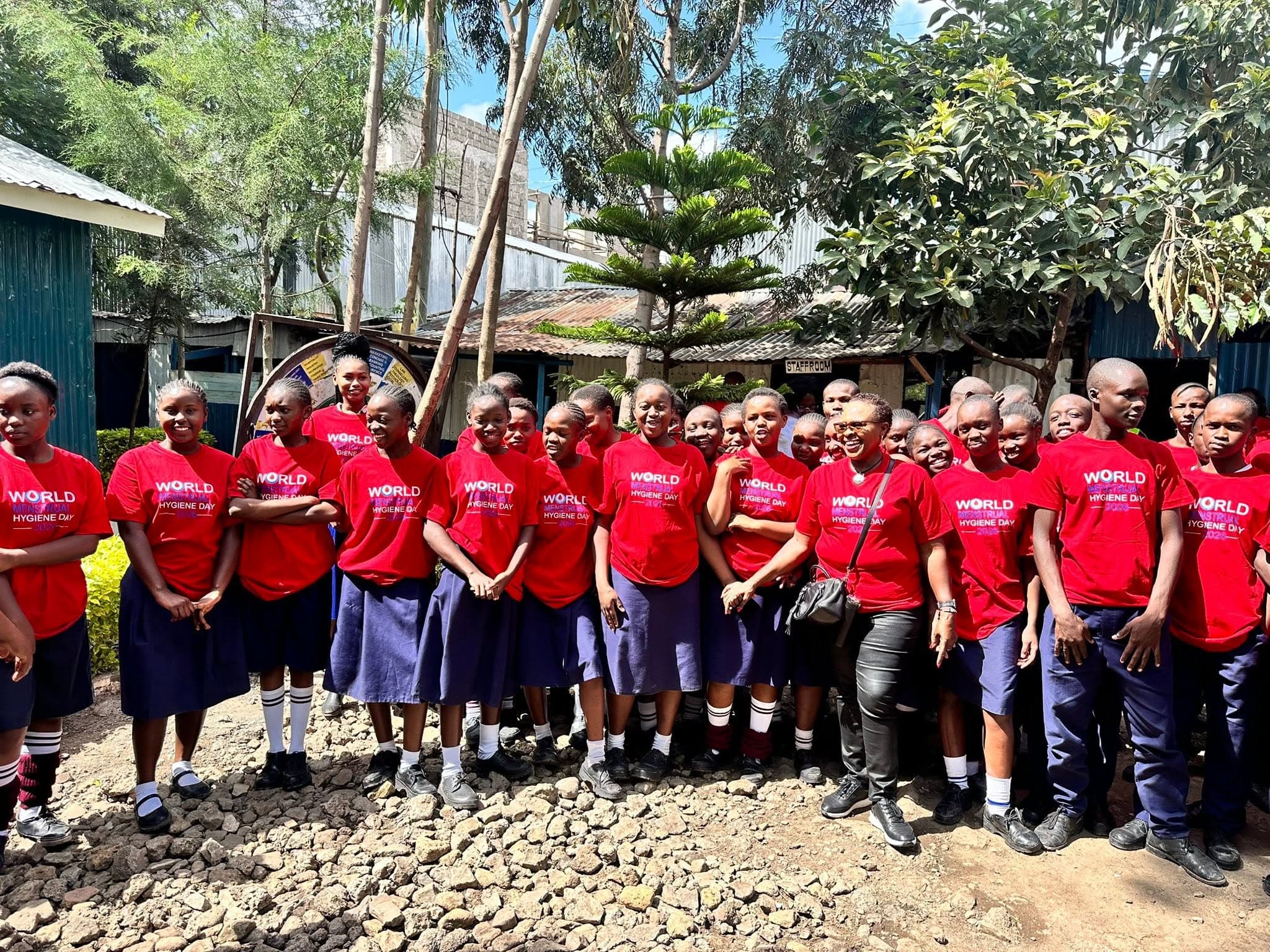 Prof. Rotich standing with students wearing red World Menstrual Hygiene Day shirts